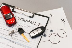 Car insurance forms and a model car sit on a cluttered desk.