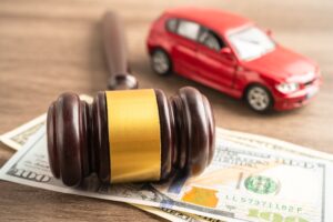 A judge’s gavel sits on several hundred dollar bills while a toy car sits out of focus.