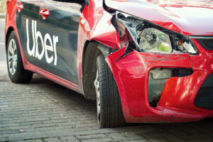 A red Uber car with noticeable damage from an accident is shown on the street, prompting the question, 'What happens if you get in an accident while driving for Uber?'. 