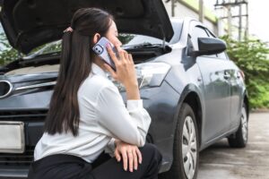A woman crouching by her car after a crash, wondering how to get compensation after a car accident.